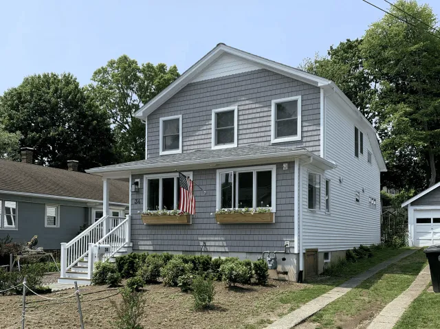 Newly renovated two-story house with gray siding and white trim in a suburban neighborhood.