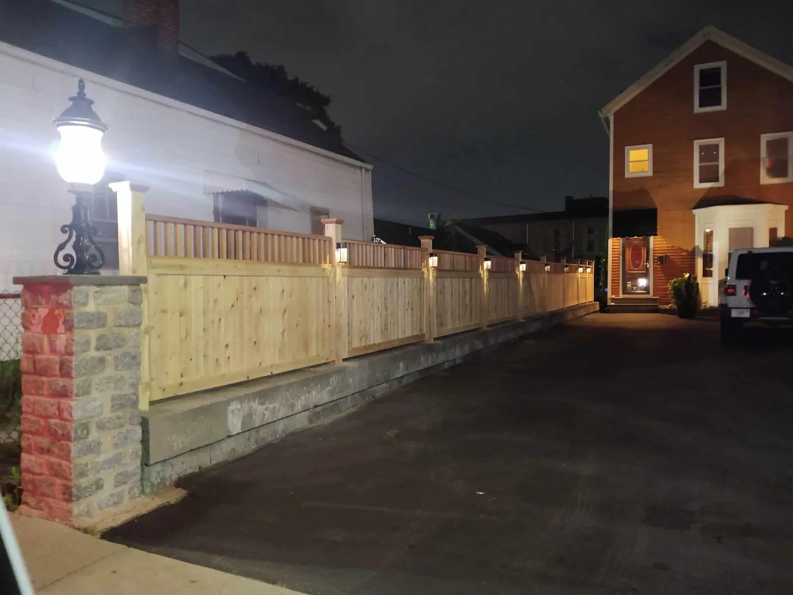 Cedar fence with lit post caps along a driveway retaining wall