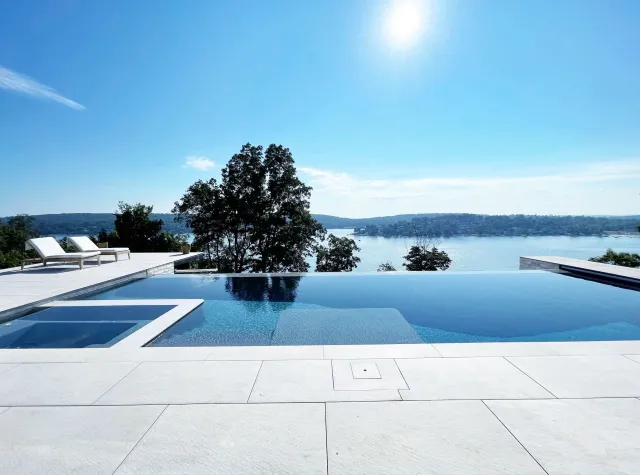 Luxury infinity pool overlooking a lake with trees and a clear blue sky.