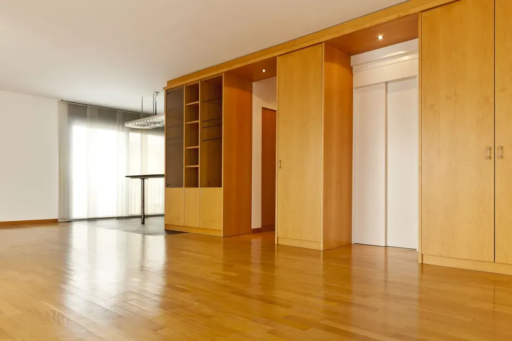 Empty, light-wood floored room with built-in cabinetry, shelving, and a white-doored elevator.