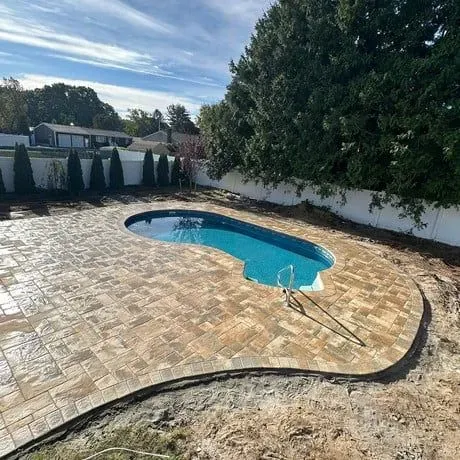 A large swimming pool is surrounded by a brick patio.