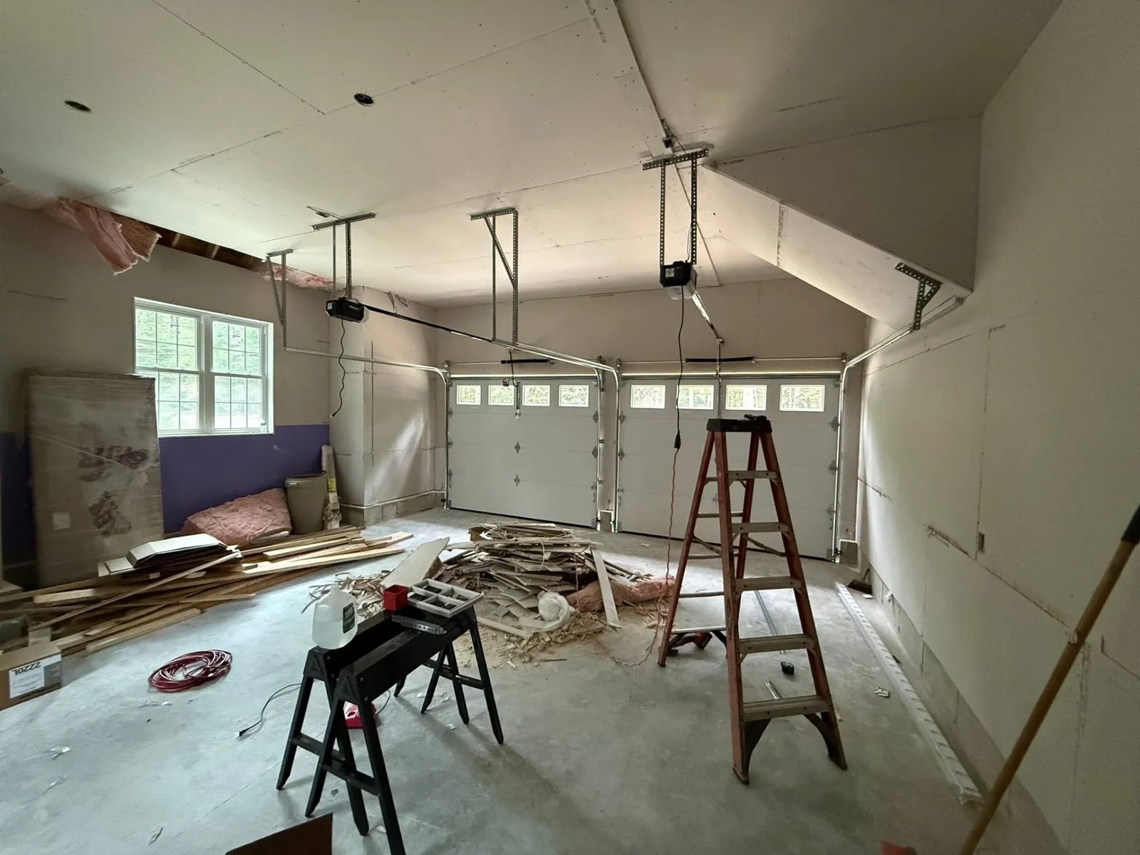 Two-car garage interior mid-installation with new sectional doors and openers being wired