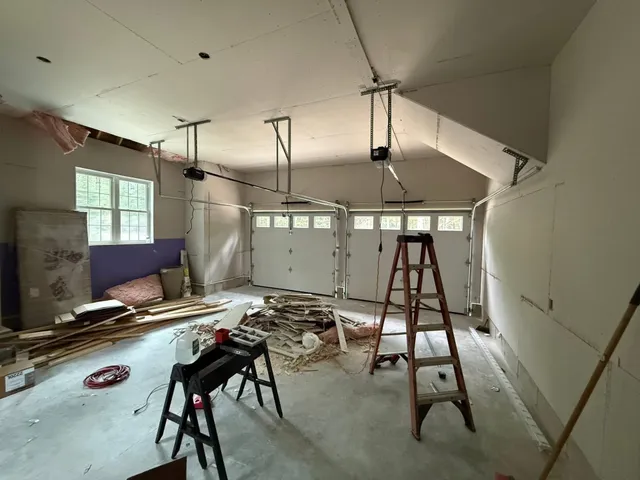 Two-car garage interior mid-installation with new sectional doors and openers being wired
