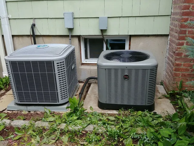 Two air conditioners are sitting outside of a house.