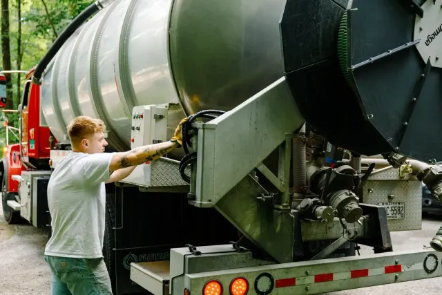 A man is working on a large septic pumping truck.