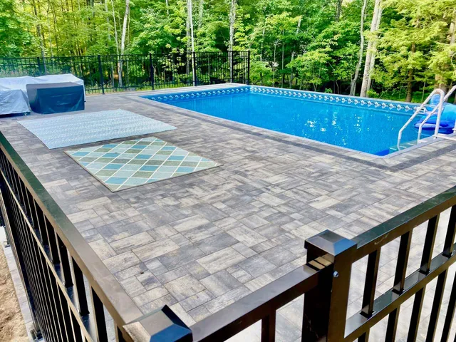 Backyard pool area with custom paver deck and secure fencing, installed by Perfect North Lawn Care in New Hampshire.