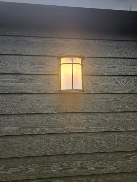 Glowing window with a cross-shaped divider, set into a weathered, gray wood-plank wall.
