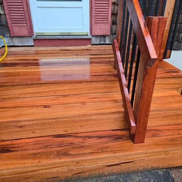 Wooden front porch with wet steps, railing, and red shutters by a house door
