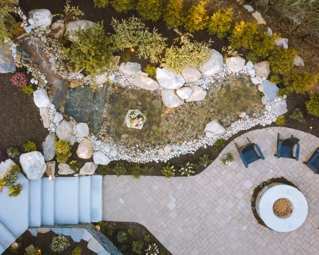 Aerial view of granite steps, water feature, pattern paver terrace, and wood-burning fire pit.