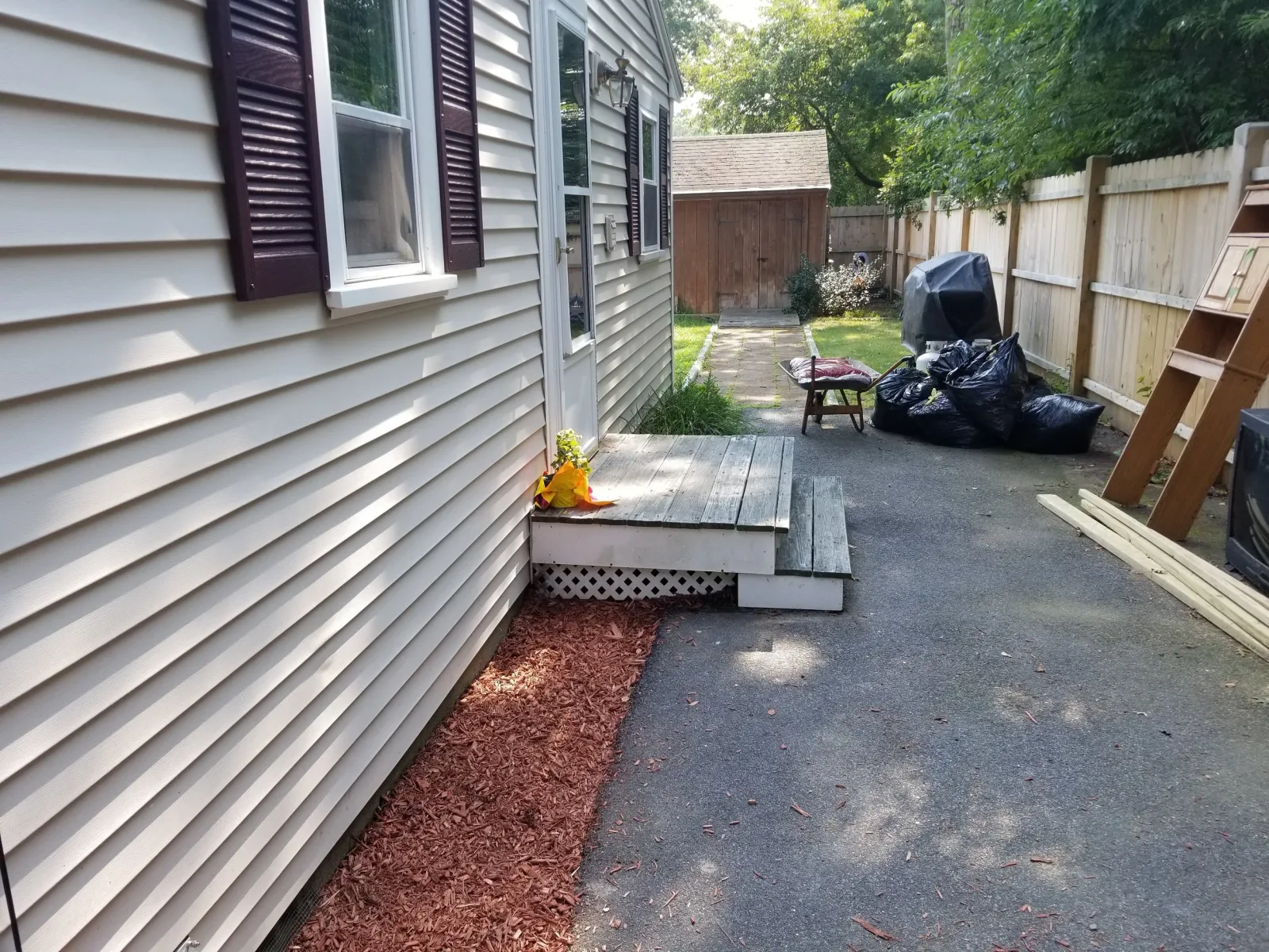 Before, side entrance of a house with a similar step in front of it, with no railing, and older looking wood.