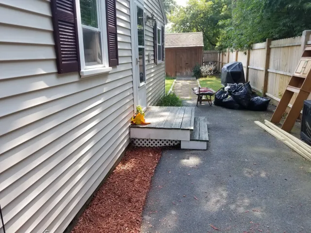 Before, side entrance of a house with a similar step in front of it, with no railing, and older looking wood.