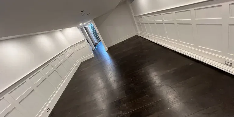 Modern renovated basement interior featuring dark hardwood floors, white wainscoting wall panels, and recessed lighting.