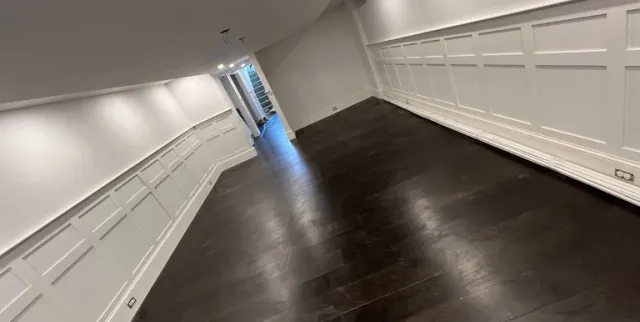 Modern renovated basement interior featuring dark hardwood floors, white wainscoting wall panels, and recessed lighting.