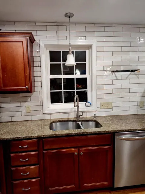 A kitchen sink area featuring dark wood cabinets, a speckled countertop, a single window with a pendant light, and tiles.
