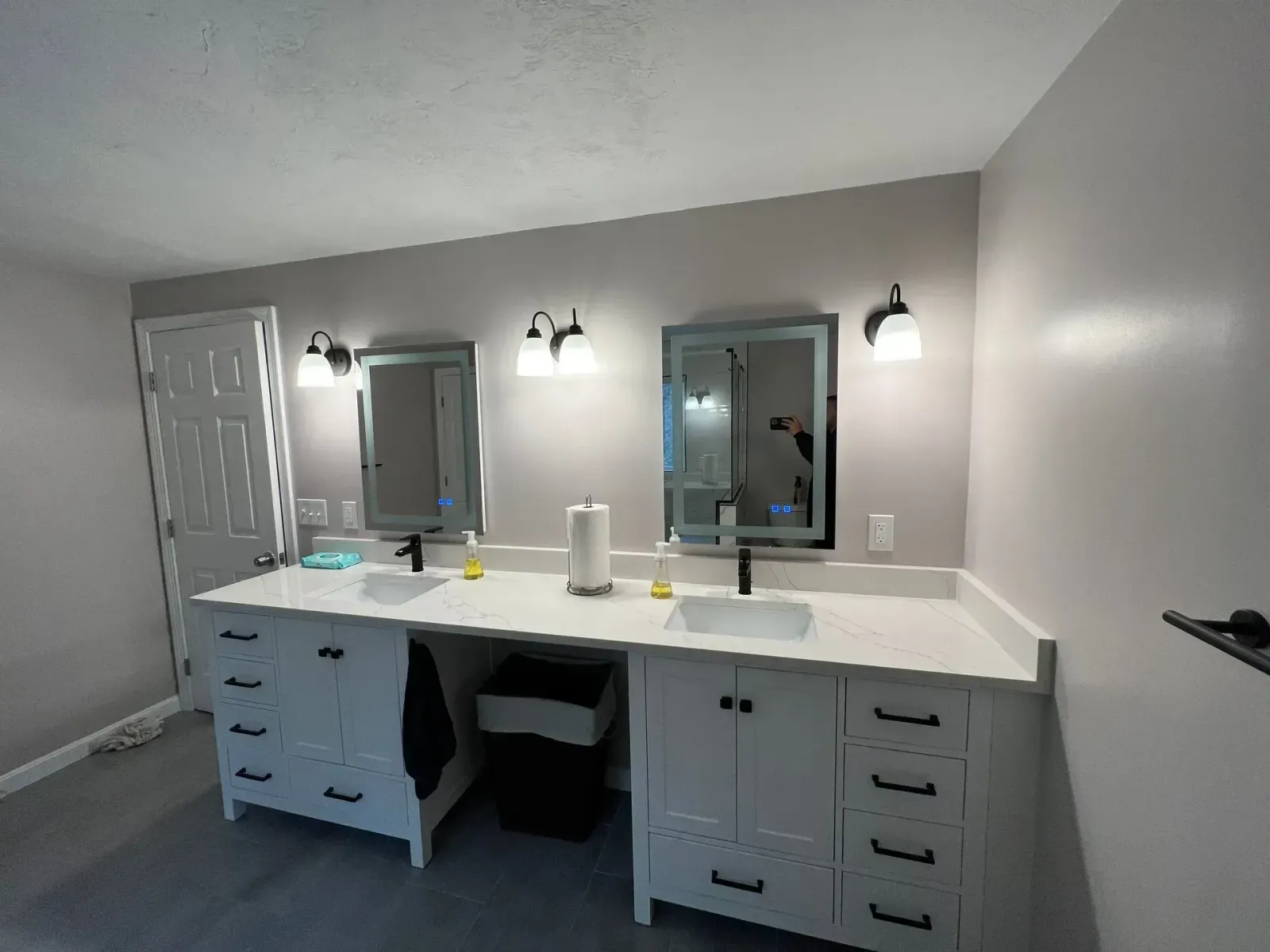 Modern bathroom vanity with double mirrors, lights, white countertop, and gray walls
