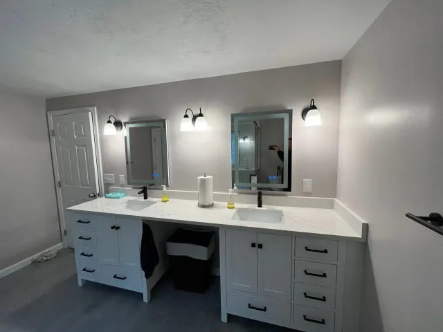 Modern bathroom vanity with double mirrors, lights, white countertop, and gray walls