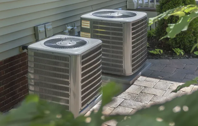 Two air conditioners are sitting on the side of a house.