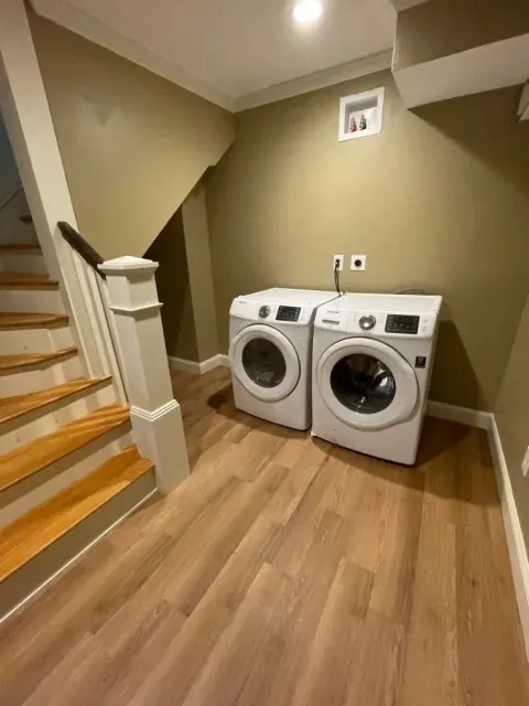 Laundry room with washer and dryer beside a staircase on a wood floor.
