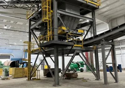 An industrial facility interior featuring large metal structures with yellow railings and machinery on the floor in the background.