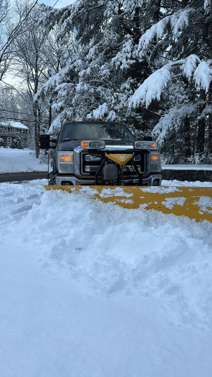 Plow truck clearing a residential driveway after a New England snowstorm