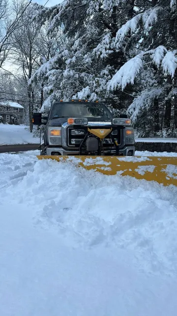 Plow truck clearing a residential driveway after a New England snowstorm