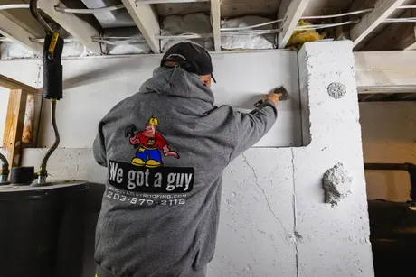 A man wearing a We Got a Guy sweatshirt is working on a wall.