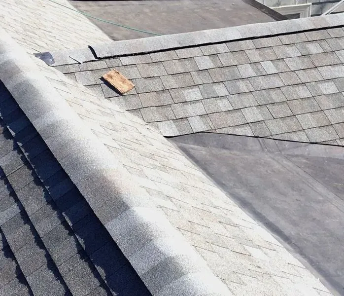 Overhead view of a weathered asphalt shingle roof, showing overlapping rows, a missing shingle, and a flat rubber section.