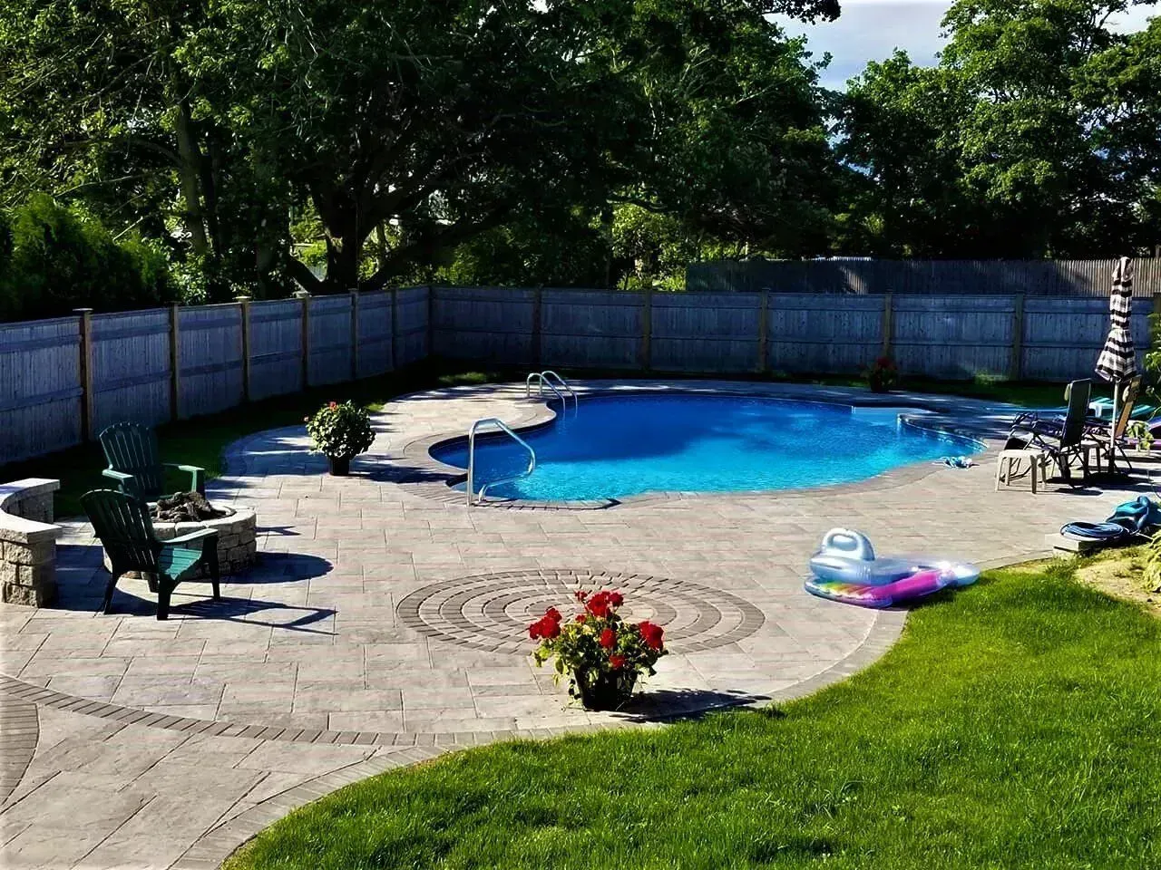 A backyard patio with flagstone paving, a small patch of artificial grass, outdoor seating, and a privacy fence.