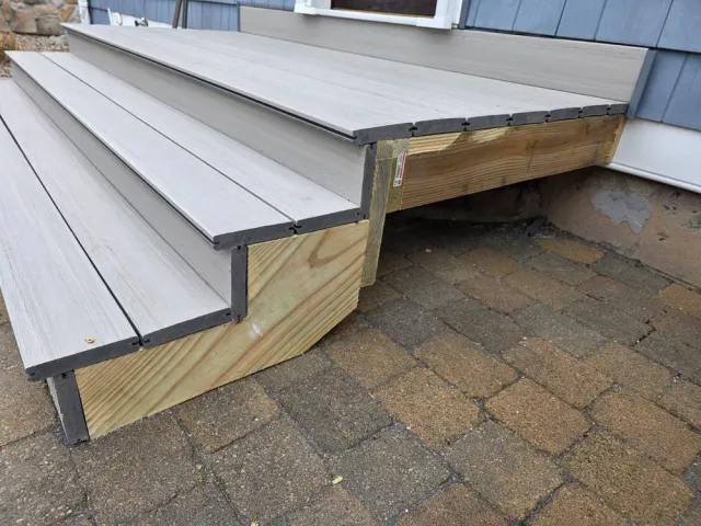 Close-up of gray stair treads with exposed wood framing on a paved patio.