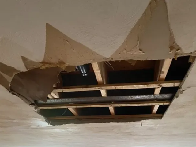 A hole in the ceiling of a room with wooden beams.