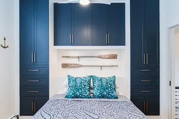 Blue built-in bedroom cabinets flanking a bed with teal pillows and patterned bedding