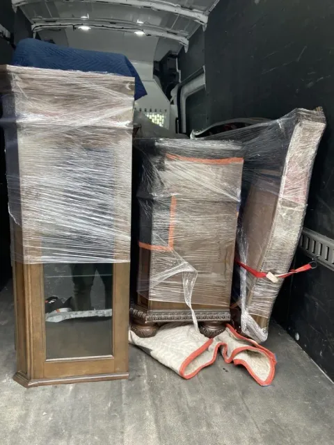 Furniture wrapped in plastic inside a van. Includes a cabinet with glass, a chest, and a tall object.