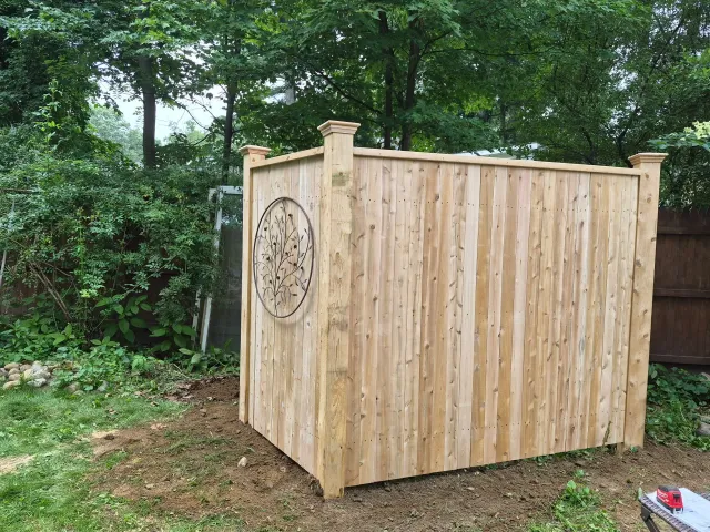 Wooden outdoor shed with a carved circular design, set in a leafy backyard.