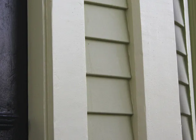 Close-up of a house corner with green siding, white trim, and black window frame.