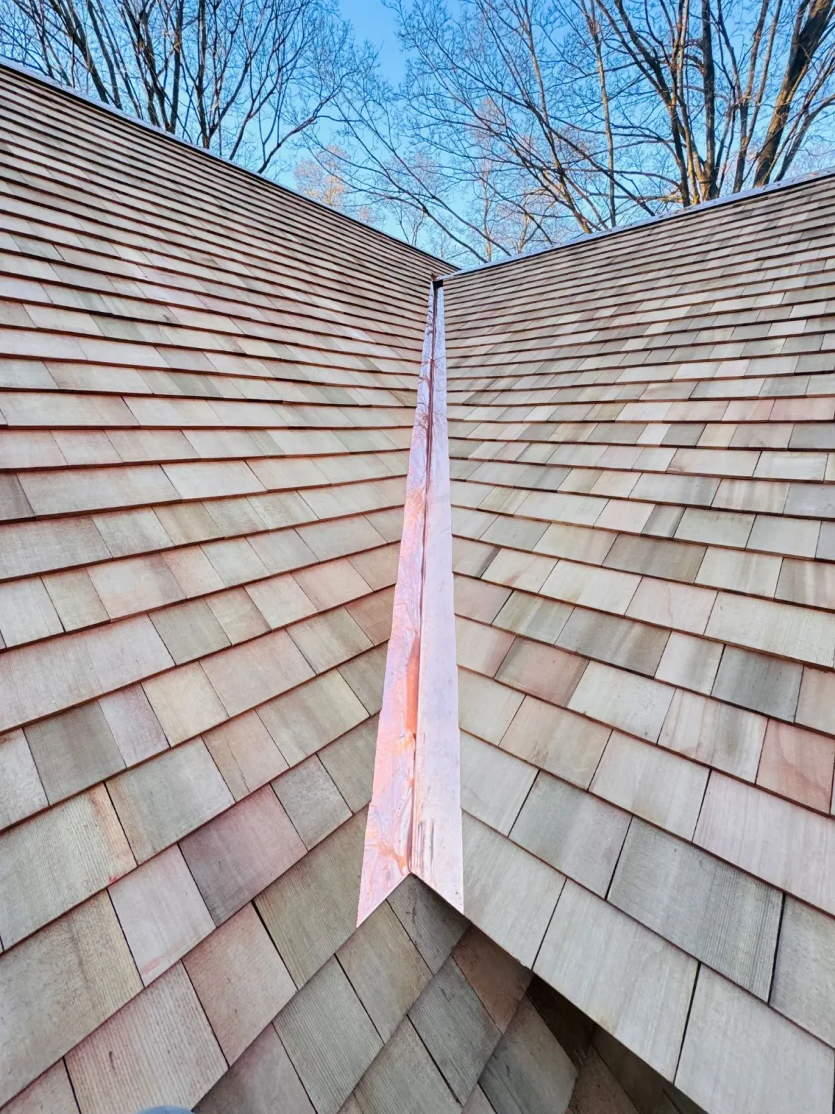 Two shingled roof slopes meeting at a central valley under a blue sky