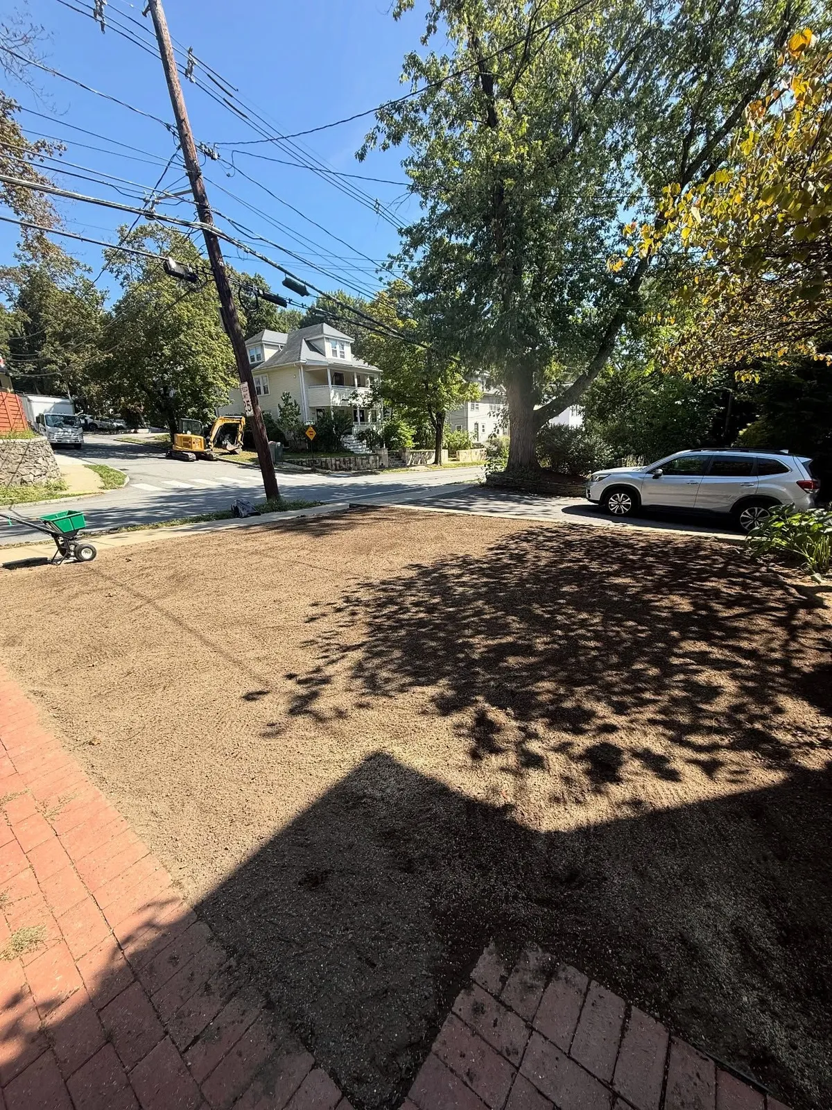 Cleared dirt patch in front yard, brick steps, street view with trees, parked SUV, and utility pole.