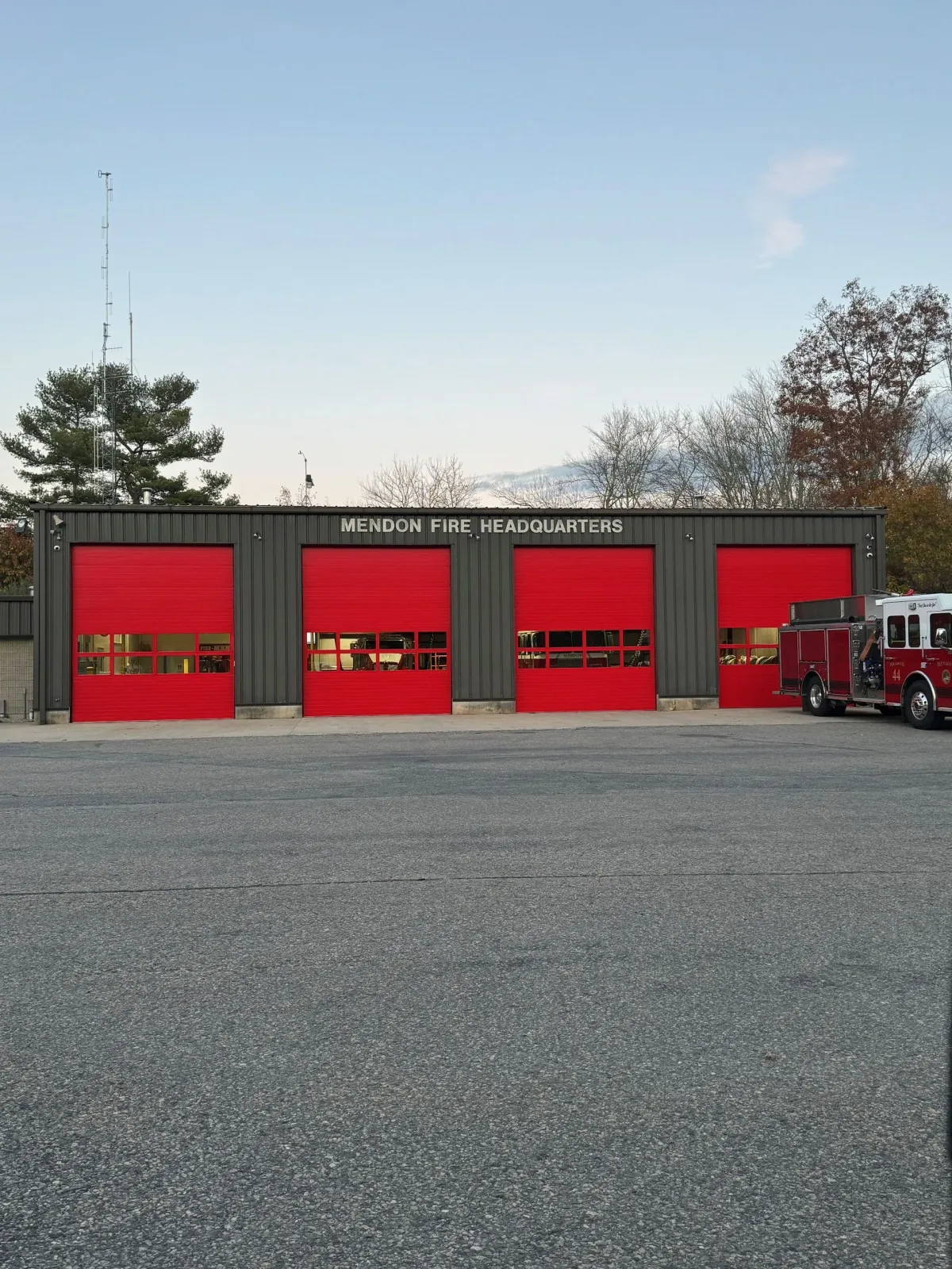 Fire station with four red garage doors, a fire truck, and a gravel parking lot.