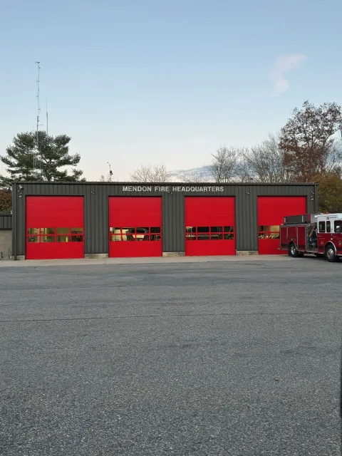 Fire station with four red garage doors, a fire truck, and a gravel parking lot.