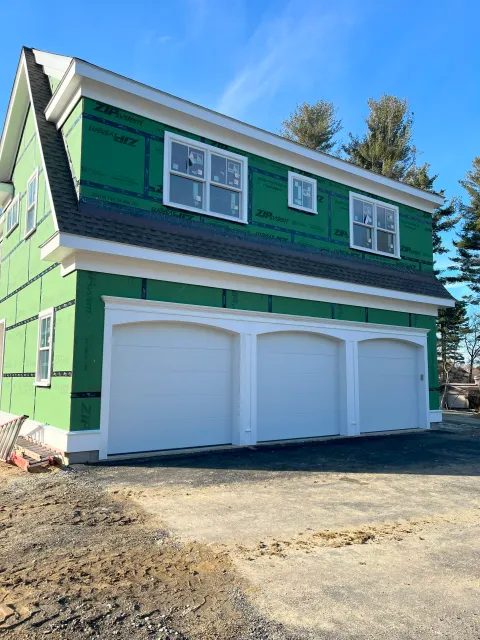 Three-car garage with white doors installed on a home wrapped in green ZIP System wall sheathing.