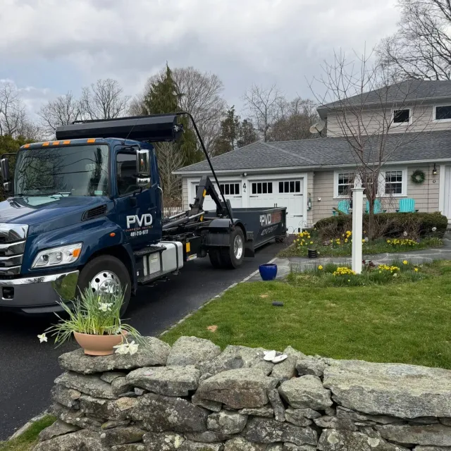 Hooklift truck picking up a dumpster from a driveway