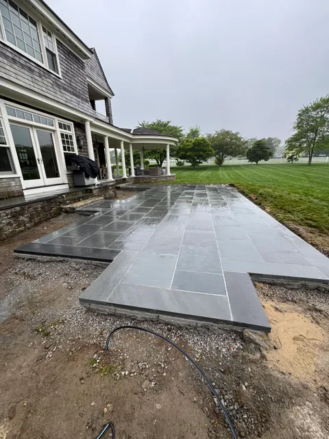 Wet stone patio under construction near shingle-sided house with white columns