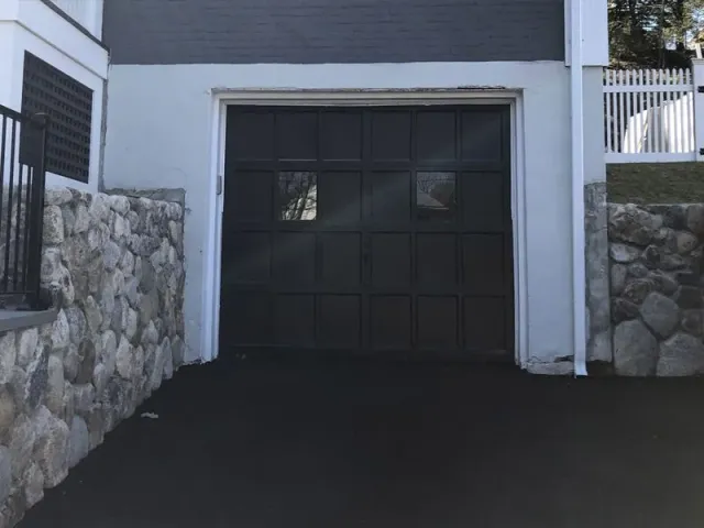 A black garage door is open next to a stone wall.