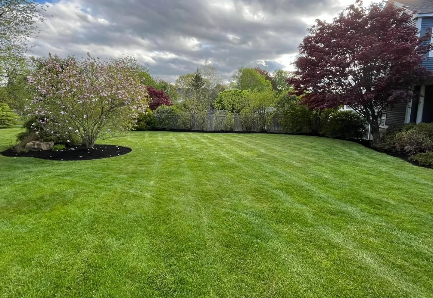 Well-manicured green lawn with flowering trees, bushes, and a cloudy sky in the background.