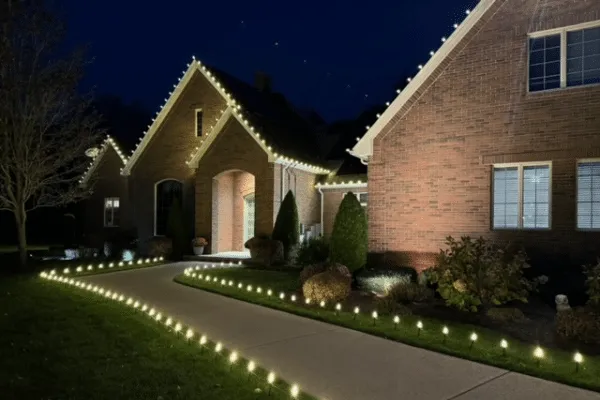 Elegant brick home illuminated with outdoor lighting and Christmas lighting outlining the roof and walkway.