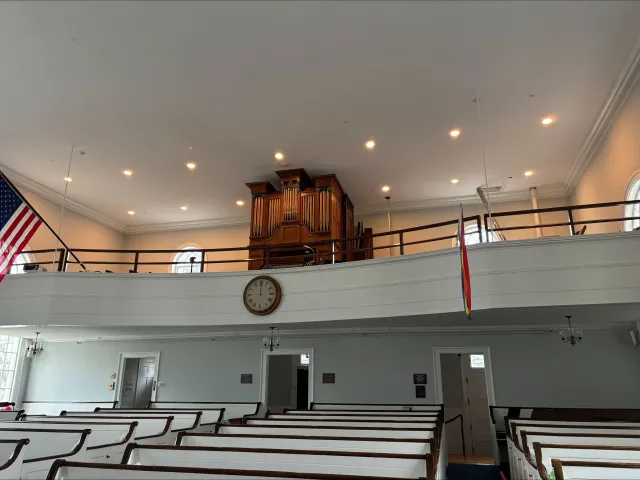 Interior of a church or chapel with pews, a clock, an organ, and flags.