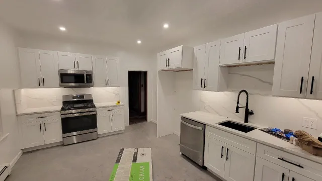 Modern kitchen with white cabinets, stainless steel appliances, black faucet, and marble countertops.