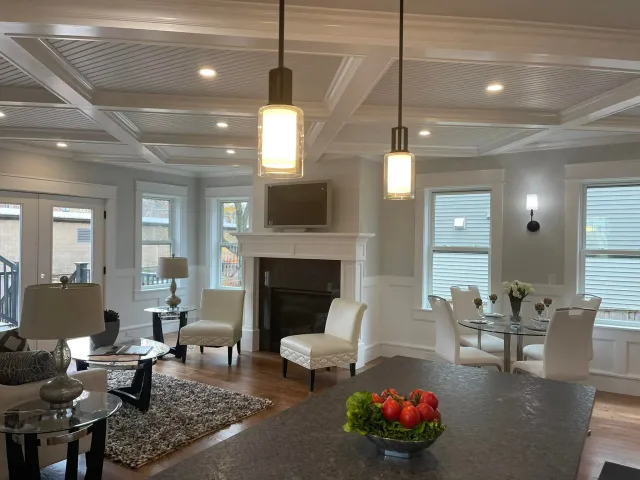 Open room under a coffered ceiling, with panel millwork, a fitted mantel and the kitchen beyond