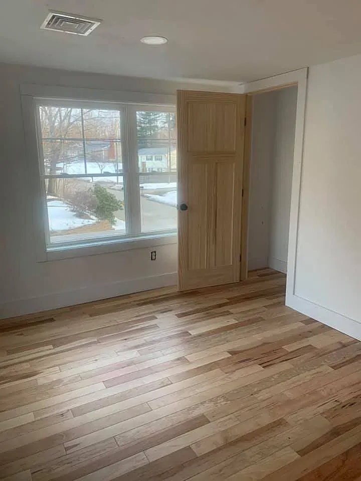An empty room with hardwood floors and a window.
