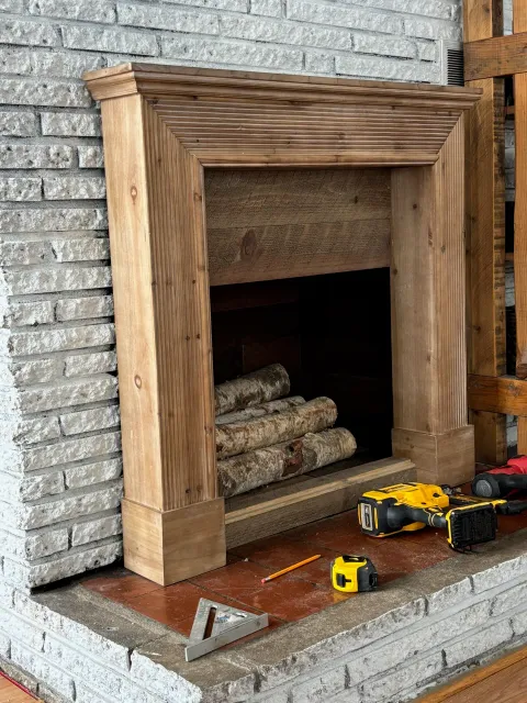 Custom wooden fireplace mantel with stacked logs and tools, showcasing interior finish work for home improvement project in Southern New Hampshire.