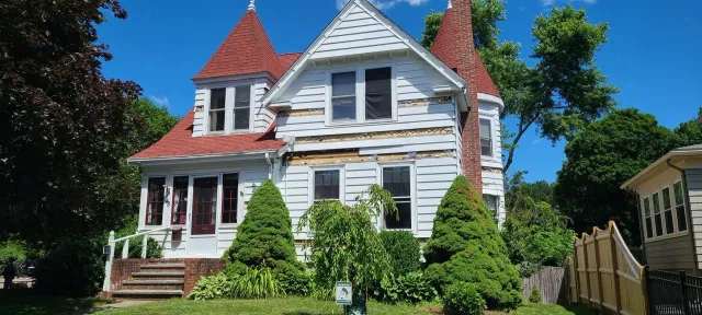White house with red roof turrets, brown chimney, green bushes, and a blue sky.